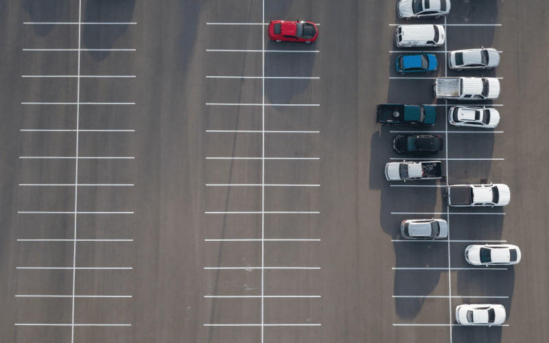 Aerial view of a parking lot with several cars parked on the right and a single red car parked on the left.