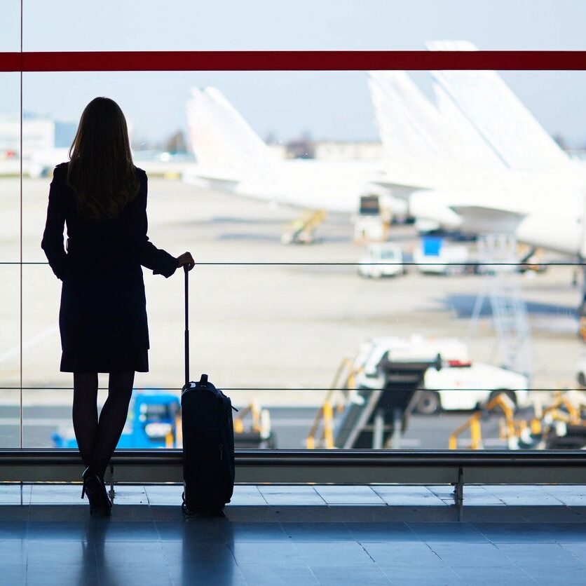 Young woman in the airport, looking through the window at planes Young woman in the airport, looking through the window at planes